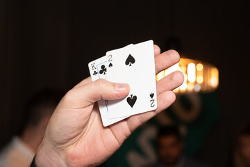 Male hand holds 2 playing cards: clubs and hearts on a dark background close-up