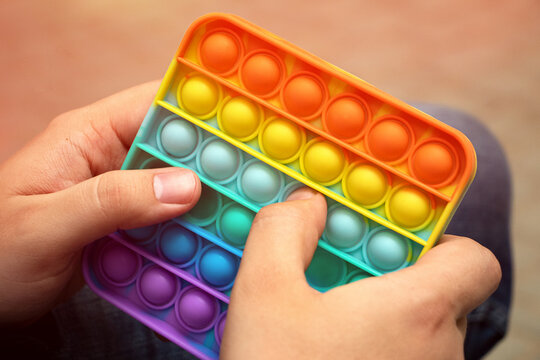 Anonymus adult hold in his hands new silcone square toy pop it.New sensory antistress toy for children and adults.Trendy rainbow coloring.