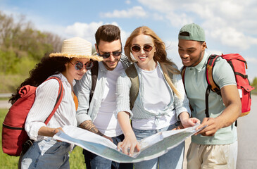 Local travel. Group of young people studying map on roadside, checking their destination point, hitchhiking for car