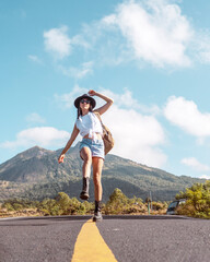 Fototapeta premium Backpacker girl walks along the road against the backdrop of a volcano and mountains. Travel concept