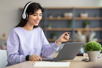 Woman sitting at desk, using computer and writing in notebook