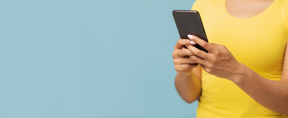 Gadget addiction concept. African american woman using smartphone over blue studio background,...