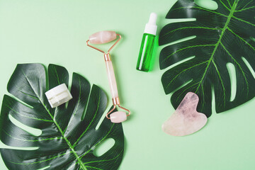 Roller and gua sha massage scraper and cometic product on a green background