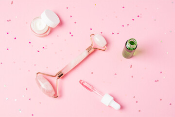 Massage quartz roller and dropper with cosmetic product on pink background