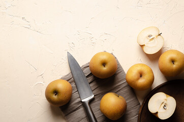 Asian pears with a silver knife on a wooden plate and a brown piece of cloth, on a light background. 