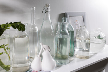 A set of bottles of different shapes with water with a photo frame is on the chest of drawers