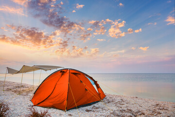 Camp tent on a beautiful quiet beach near the water against  the sunset sky background