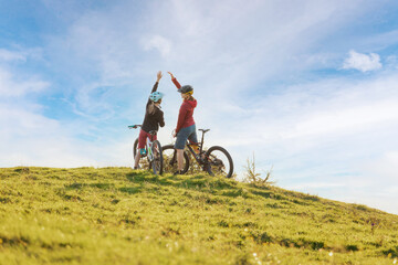 Two happy woman high five over the sunset after a successful mountain biking trip in the mountains....
