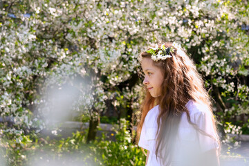 beautiful teenage girl with long blonde hair in white clothes enjoys the spring cherry blossom. A flower in her hair. Copy space