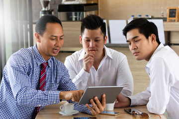 Businessmen or success business team sitting and meeting at table in coffee shop and discuss business plan. On table tablet, smartphone, cup of coffee.