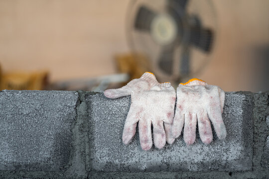 A pair of dirty cotton glove for building worker is hanging on the brickwall during the staff taking a rest. Industrial object photo. Partail focus at the glove part