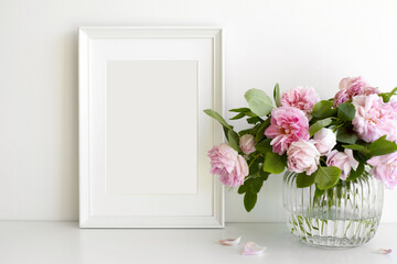 Indoor image of pinkish peony flowers arranged in vase on table with vertical rectangular photo frame with copy space for your picture or design. Home, decoration, interior and memory concept
