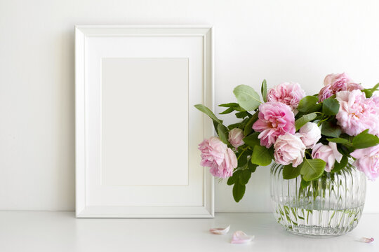 Indoor image of pinkish peony flowers arranged in vase on table with vertical rectangular photo frame with copy space for your picture or design. Home, decoration, interior and memory concept