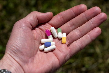 Own hand holding colorful pills at sunlight.