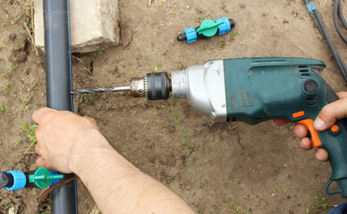 Close-up - hand drills a hole in the pipe. Installing drip irrigation in a farm with your own hands. Assembly of the drip irrigation system. Irrigation system. Drip Irrigation Plug. drip tape fittings