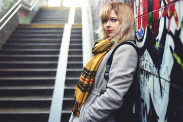 Beautiful girl standing near a wall with graffiti in underground passage