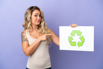 Young Brazilian woman isolated on purple background holding a placard with recycle icon and  pointing it
