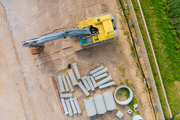 Small excavator at stacked concrete drainage pipe on construction site © ungvar