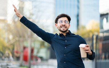Young man holding a cup of coffee and calling a taxi outdoors.