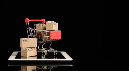 Shipping paper boxes inside Red shopping cart trolley on tablet with black background and copy space , Online shopping and e-commerce concept.