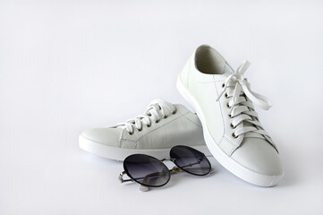 White stylish women's sneakers and sunglasses isolated on a white background. Summer shoes for sports and recreation. Copy space