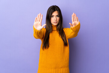Teenager Brazilian girl over isolated purple background making stop gesture and disappointed