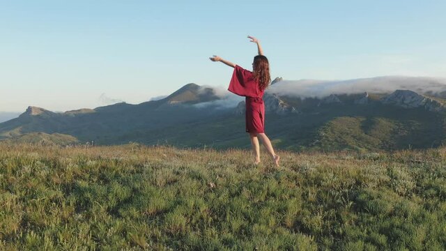 A view of a woman performing a ritual dance on a hilltop in the rays of sunset against a background of mountains covered with white fog