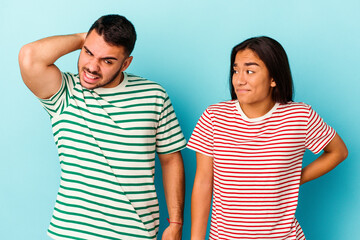 Young mixed race couple isolated on blue background touching back of head, thinking and making a choice.