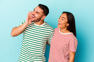 Young mixed race couple isolated on blue background shouting and holding palm near opened mouth.