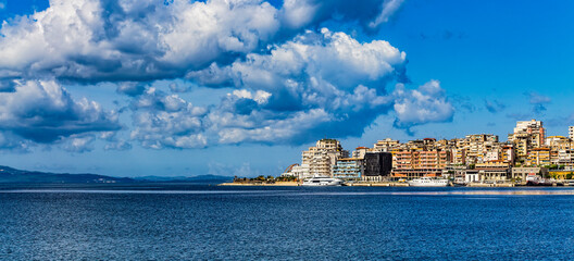 Panoramic view of Saranda bay and town and city port along the coast, Albania. Sunny summer day. Beautiful clouds in the sky. Corfu island visible on the horizon. Calm blue sea.