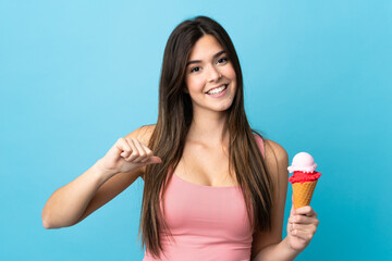 Teenager Brazilian girl holding a cornet ice cream over isolated blue background proud and self-satisfied