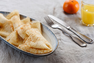 Breakfast with crepes or pancakes and jam, juice and tangerine on greige linen tablecloth. Pancake week or Shrovetide. Selective focus