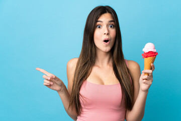 Teenager Brazilian girl holding a cornet ice cream over isolated blue background surprised and...