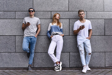 Fototapeta premium Fashion portrait of Three best friends posing at street, wearing stylish outfit and jeans against gray wall .