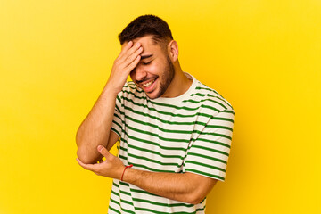 Young caucasian man isolated on yellow background blink at the camera through fingers, embarrassed covering face.