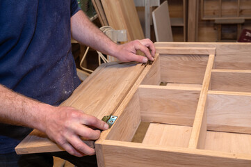 hands of a master carpenter set the hinges on the cabinet. Production of handmade wooden furniture....