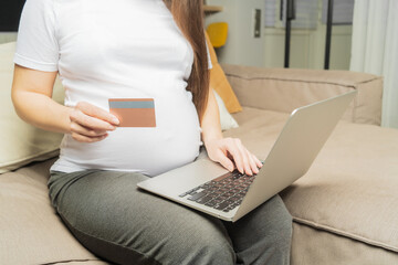 Online shopping on the Internet. Pregnant girl at the computer, pays for children's shopping with a card