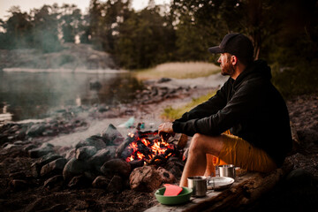 Side view of mature man sitting by campfire while looking away during sunset