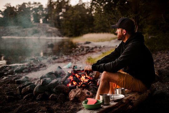 Side view of mature man sitting by campfire while looking away during sunset