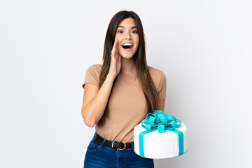 Teenager pastry chef holding a big cake over isolated white background shouting with mouth wide open