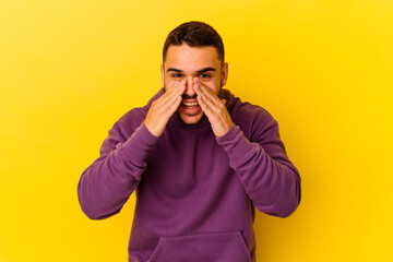 Young caucasian man isolated on yellow background saying a gossip, pointing to side reporting something.