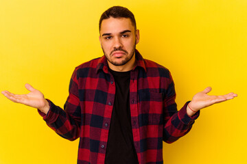Young caucasian man isolated on yellow background doubting and shrugging shoulders in questioning...