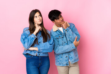Young couple over isolated pink background thinking an idea while looking up