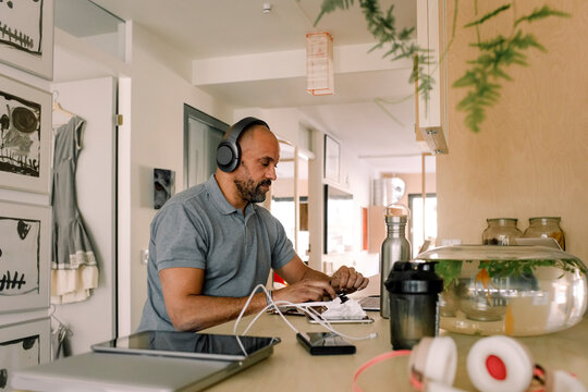 Businessman wearing headphones working on laptop while sitting at kitchen island