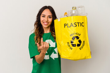 Young mexican woman recycling plastic isolated on white background pointing with finger at you as if inviting come closer.