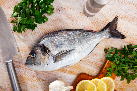 Uncooked dorado fish with lemon, garlic and parsley on wooden table. High quality photo