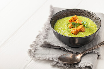 Green peas soup with breadcrumbs in a bowl on a white wooden table. Copy space