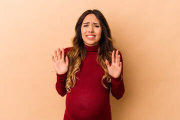 Young mexican pregnant woman isolated on beige background rejecting someone showing a gesture of...