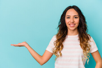 Young mexican woman isolated on blue background showing a copy space on a palm and holding another...