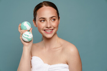 Ginger woman wearing towel smiling while showing balls bath bomb